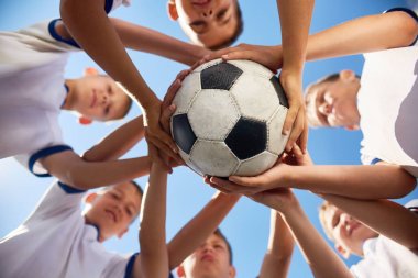 Düşük açılı görünüş genç futbol çocuklardan daire holding topu birlikte mavi gökyüzü karşı ayakta takım, topa odaklanmak