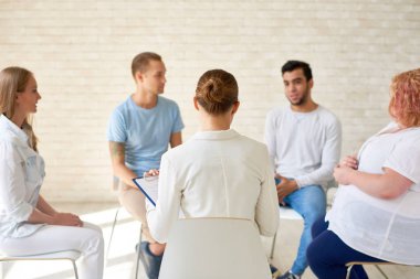 Arkadan görünüşü kadın Koç grup terapi seansı veya ışık geniş oda Eğitim Semineri sırasında daire içinde oturan genç insanlar ile çalışma