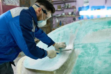 Portrait of unrecognizable mature man wearing protective mask repairing boat while working in yacht workshop, covering boat with pre-paint base coating,  copy space clipart