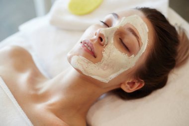 Mutlu genç kadın zevk güzellik bakımları ve Spa yüz maskesi portre portre, gözleri ile masaj masanın üzerinde yatan kapalı