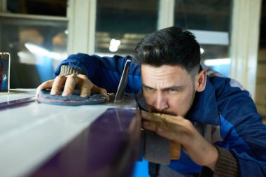 Portrait of handsome man polishing surfing board with felt disk in yacht workshop, copy space clipart