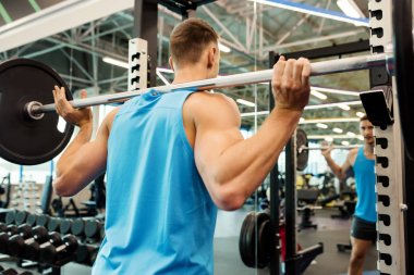 Modern spor salonunda egzersiz sırasında ağır barbell ile egzersiz yapan silah kasları pompalayan güçlü adam geri görünümü