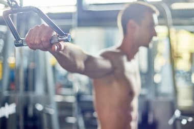 Yan görünümü kullanan yakışıklı kaslı adam portresi makine kolu tutan güçlü el üzerinde odaklanmak modern bir spor salonu, makinede egzersiz