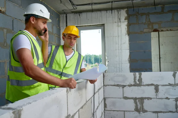 Porträtt Två Byggnadsarbetare Bära Hardhats Diskutera Planlösningar Inuti Halvfärdig Byggnad — Stockfoto