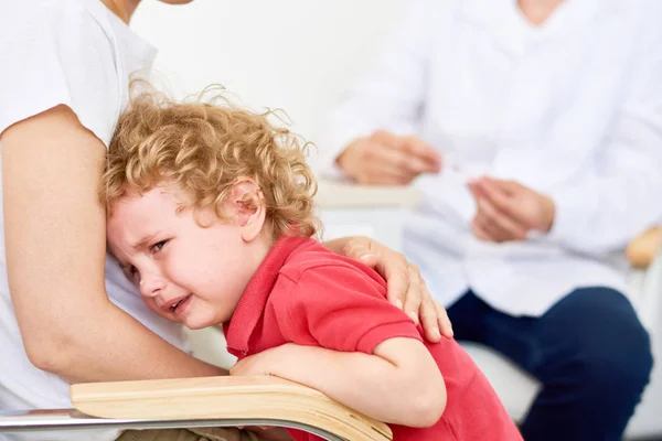 Portrait of crying  little boy hugging mother during appointment with doctor