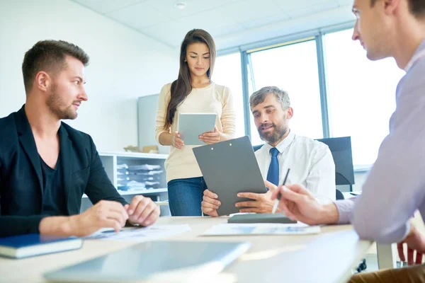 Multi-ethnic team of managers analyzing results of accomplished work while gathered together at spacious meeting room with panoramic windows