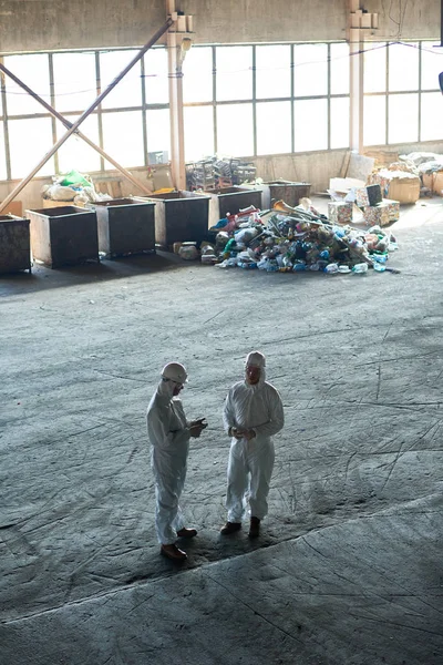 廃棄物処理プラント バック グラウンド コピー スペースでゴミの山の空のワーク ショップに立って倉庫スーツを着た 人の労働者に高角度を表示します — ストック写真