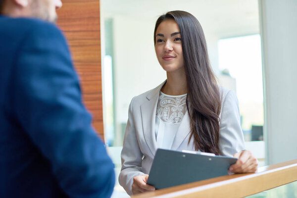 Portrait of young Asian businesswoman smiling happily while chatting with unrecognizable colleague standing at glass balcony in modern office building