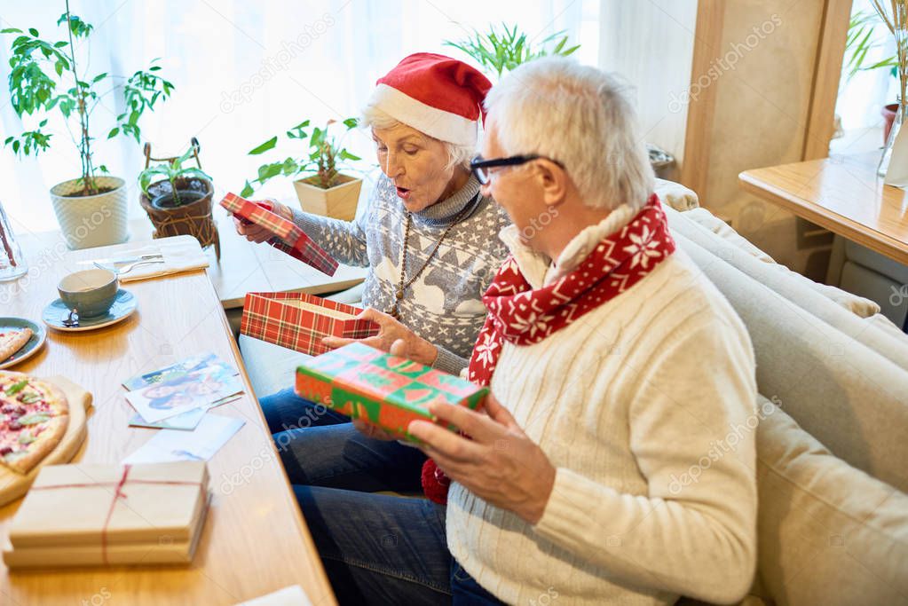High angle portrait of loving senior couple opening christmas presents and laughing happily sitting at cafe table with family, copy space