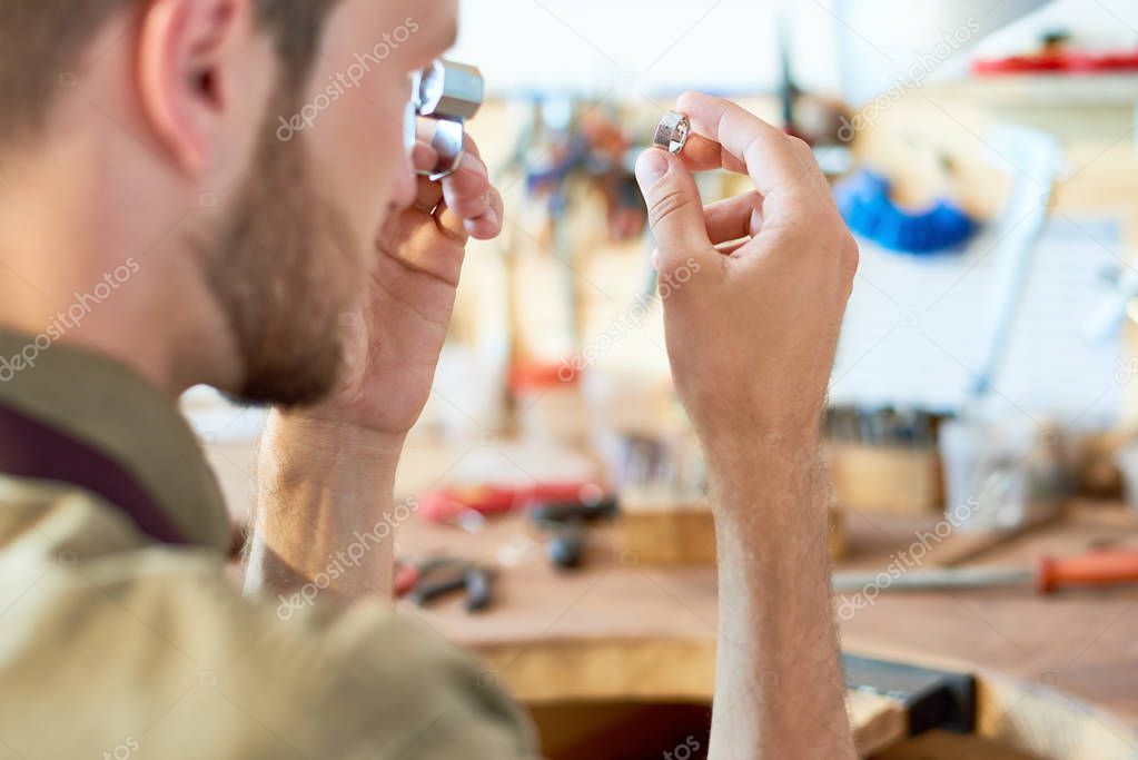 Portrait of jeweler inspecting ring through magnifying glass in workshop