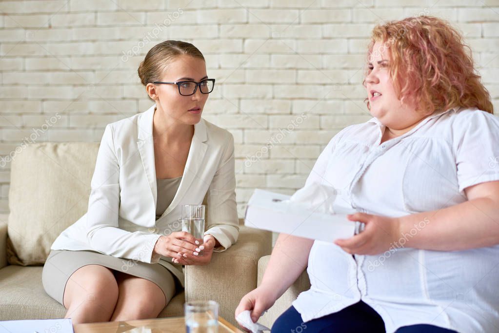 Portrait of crying overweight woman  sharing mental issues with female psychiatrist during therapy session  in doctors office