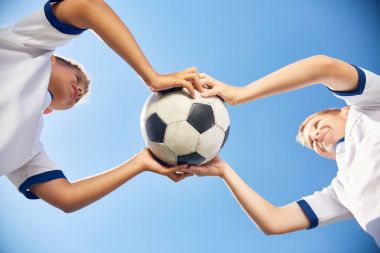 İki erkek genç futbol takımı karşı açık mavi gökyüzü topu tutan düşük açılı portresi
