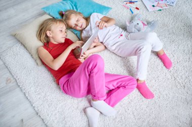 Sevimli küçük arkadaş geniş oturma odası rahat halı üzerinde yalan sırasında dijital tablet eğitim programı izlerken yüksek açılı görünüş