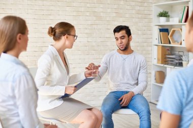 Kadın psikiyatrist bardak su için genç adam çevrelerindeki bir dairede oturan diğer hastalarla grup terapisi oturumda teslim portresi