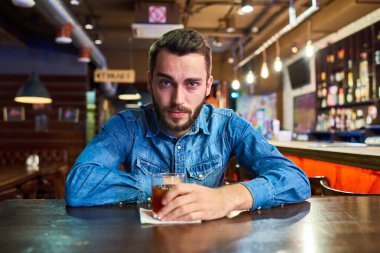 Alkol cam ile barda masada oturan kırmızı şiş gözler ile kameraya bakarak sarhoş genç adam portresi