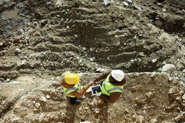 Üstten görünüm açık havada dijital tablet, kopya alanı kullanarak madenciliği iş sitesi üzerinde duran el sıkışan yansıtıcı ceket giyen iki endüstriyel işçilerin vurdu