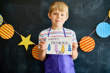 Babalar okulda blackboard karşı poz ve kameraya bakarak günü için el yapımı kart tutan şirin küçük çocuk portresi