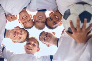 Düşük açılı portre ısıtmaz ve kamera karşısına mavi gökyüzü gülümseyen daire içinde duran genç futbol takımı