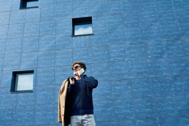 Telefonla konuşma ve mutlu gri beton duvara, kopya alanı caddenin ayakta gülümseyen güneş gözlüğü takıyor yakışıklı genç adam portresi düşük açılı