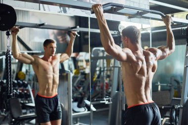 Modern spor salonunda yoğun egzersiz yaparken ayna önünde pazı için egzersiz yapan çıplak gövde ile Yakışıklı genç vücut geliştirmeci