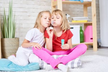Birlikte kalın halı evde katta oturan kabarcıklar üfleme iki sevimli küçük kız portresi