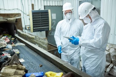 İki işçi biohazard giyen portresi işleme çöp sıralama ve dijital tablet ayakta Konveyör bant, kopya alanı kullanarak tesisi atık çalışmaya uygun