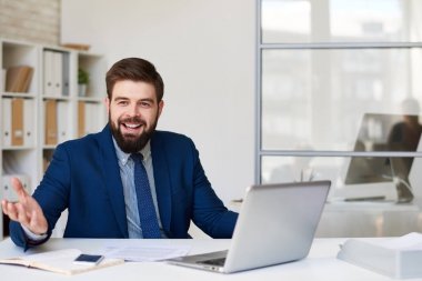 Mutlu bir şekilde modern ofis masasında çalışırken gülümseyen başarılı sakallı işadamı portresi