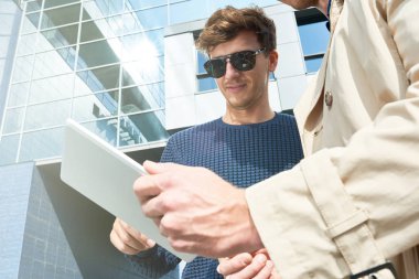 Açı portre iki başarılı genç adamın dijital tablet açık havada duran ofis binası, modern karşı kopya alanı kullanarak düşük