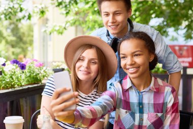 Çok etnik gruptan oluşan gençlerin grup smartphone selfie açık kafede güneşli yaz gününde alarak üç mutlu