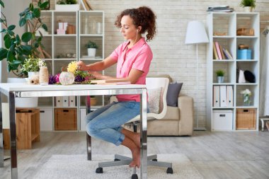 Yan görünüm portre genç kadının güzel çiçek kompozisyon zanaat, kopya alanı zevk müzik dinlerken modern daire masasında yapma