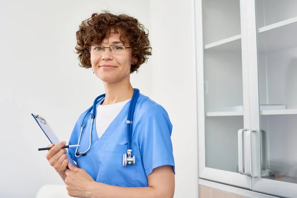 Retrato Una Joven Médica Sonriendo Alegremente Cámara Posando Oficina Sujetando — Foto de Stock