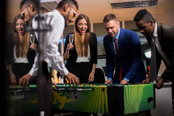 Young company workers drinking alcohol beverages, playing table football and having fun on Friday office party