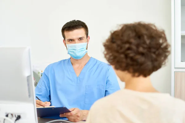 Retrato Joven Médico Con Máscara Facial Hablando Con Paciente Consultorio — Foto de Stock