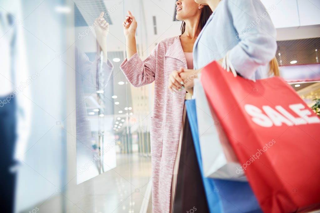 Mid section portrait of two beautiful women in shopping center looking at window displays of store and smiling, choosing clothes