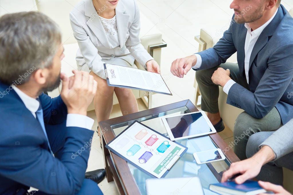 High angle view at group of successful business people working together in modern office focus on coffee table with charts, graphs and contract
