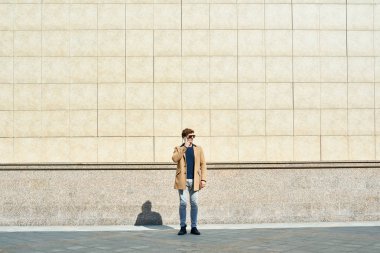 Tam uzunlukta kopya alanı açık havada, duvarın ayakta telefonla konuşan bir sonbahar palto giyiyor modern genç işadamı portresi
