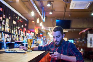Portre sakallı modern sayaç smartphone kullanarak pub bar, oturan adam ve bira içme alanı Kopyala