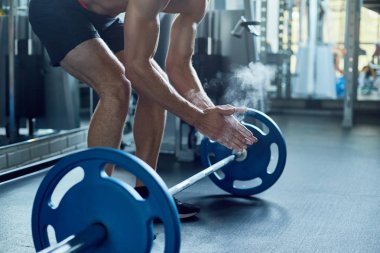 Geniş spor salonunda halter kaldırma için hazırlarken tebeşir ile el kapsayan tanınmaz halde genç vücut geliştirmeci