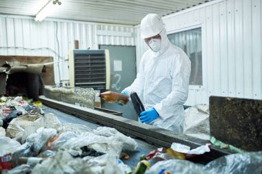 Biohazard takım ve hardhat geri dönüşümlü malzeme Konveyör bant üzerinde sıralama atık işleme tesisinde çalışan işçi portresi
