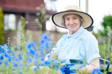 Güzel eski Çiçek bahçesinde poz hasır şapka giyen kadın kamera çalışırken gülümseyen portresi