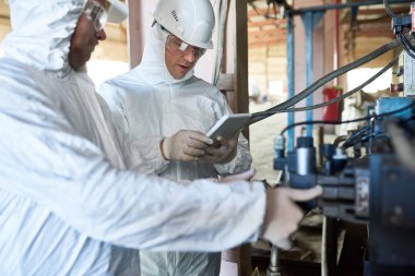 Portre, makine üzerinden dijital tablet üzerinde modern işleme tesisi işletim biohazard takım elbise giyen iki fabrika işçi