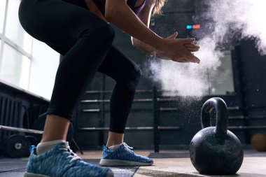 Yan görünümü closeup tanınmaz halde genç kadının ellerini ovuşturarak konuşmak şişirme bulut modern bir spor salonu crossfit egzersiz sırasında kettlebells kaldırmaya hazırlanıyor