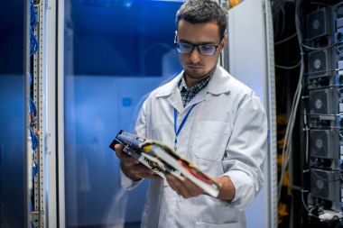 Laboratuvar önlüğü ve gözlük süper bilgisayarla çalışırken blade sunucu tutan genç adam portresi