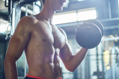 Pazı dumbbells ile geniş spor salonunda, arka plan bulanık yoğun bir eğitim yaparken bina terli kaslı adam görünümünü profil