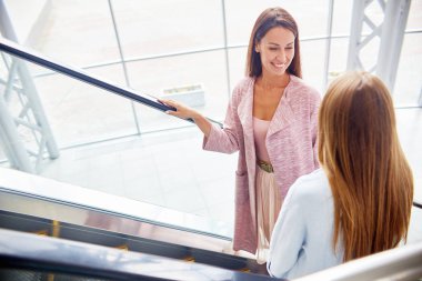 Sohbet ve mutlu bir şekilde giderken gülümseyen iki genç kadın alışveriş merkezi, yürüyen merdiven üzerinde yüksek açı