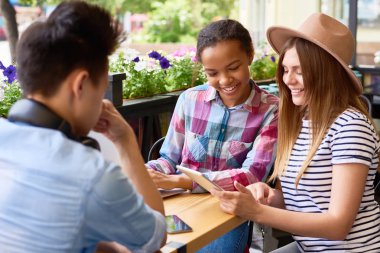 Çok etnik gruptan oluşan grup üç arkadaşıyla birlikte dijital tablet açık kafede güneşli yaz gününde kullanma.