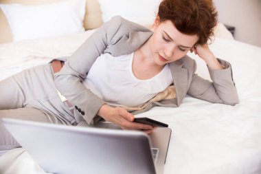 Oldukça genç işkadını telefonunu kontrol ve, dizüstü bilgisayar kullanarak otel yatağa atma iş seyahat konaklamanın tadını portresi