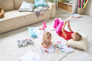 Serbest zaman evde harcama: sevimli küçük kız rahat halı üzerinde yalan ve Keçeli Kalemler süre iskambil spor dijital tablet üzerinde onun ablası ile resim boyama