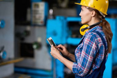 Yan görünümü ile modern fabrikasında makine çalışırken dijital tablet kullanarak kadın makine operatörünün portresi