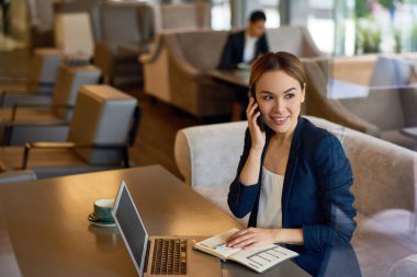 Onun iş ortağı için rahat küçük kafede, bel, dikey otururken smartphone üzerinde konuşmak çekici genç Yöneticisi